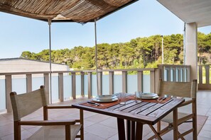 Une table en bois, dressée pour deux personnes, avec des chaises, un chemin de table en fibres tressées et une vue sur une colline boisée.