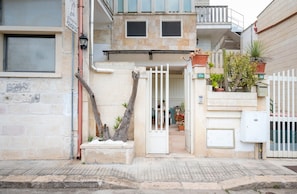 Ein Gebäude mit geschlossenem Eingangsbereich, Blumentöpfen und einem sichtbaren Balkon.