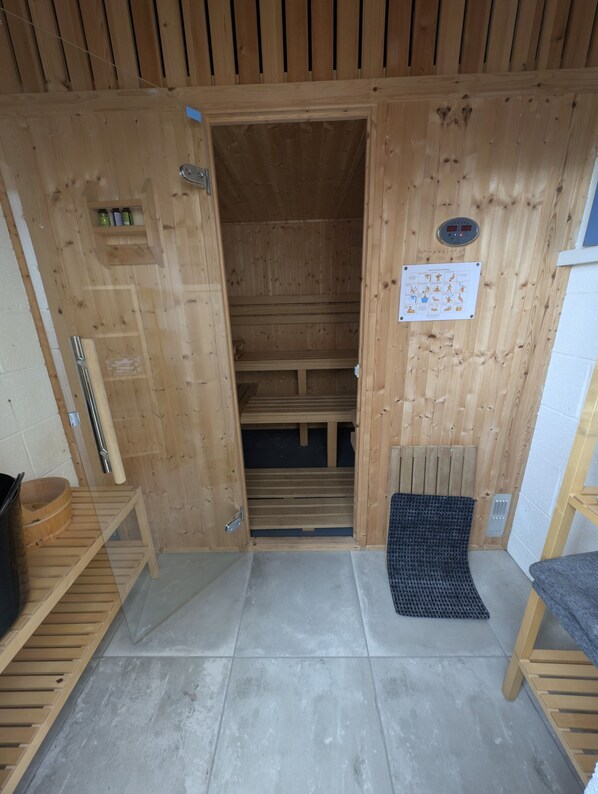 A wooden sauna with a bench, a small shelf with bottles, and a mat at the entrance.