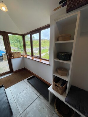 A room with a large window, a white shelving unit with baskets, and a bench.