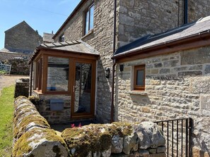 Un bâtiment en pierre avec une porte et une fenêtre en bois, un mur en pierre et un portail en métal.
