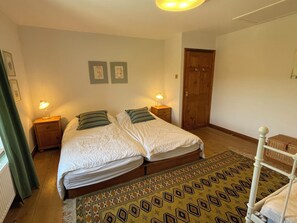 A bedroom with a double bed, two bedside tables with lamps, a wooden door, and a patterned rug.