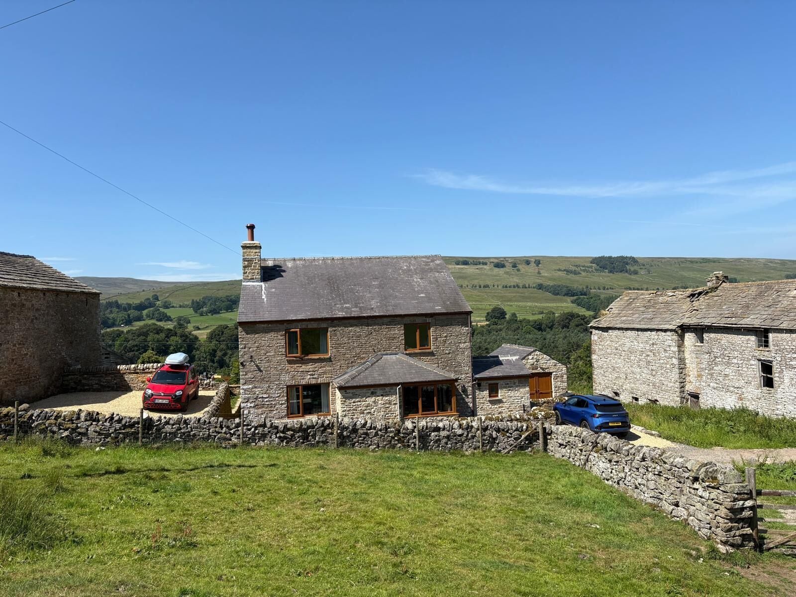 A stone house with a chimney, a red car, and a blue car parked in front.