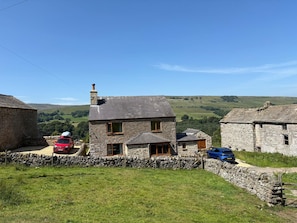 A stone house with a chimney, a red car, and a blue car parked in front.