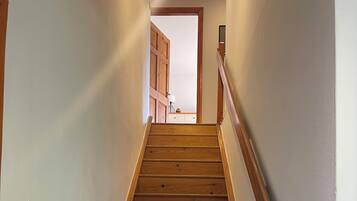 Eine Holztreppe mit Handlauf, die zu einem Raum mit Tür und Lampe führt.