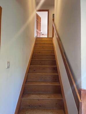 A wooden staircase with a handrail, leading to a room with a door and a lamp.