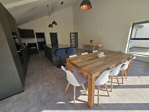 A modern kitchen with a central island, a dining area with a wooden table and white chairs, and pendant lighting. - Luxury Kent Bungalow Retreat Sleeps 12 (Tonbridge)