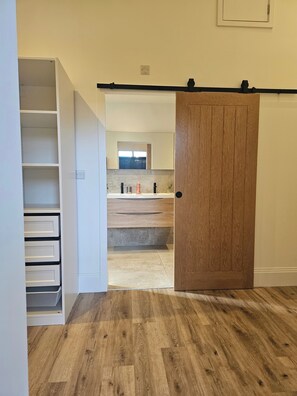A room with a wooden floor, a white wardrobe, and a door leading to a bathroom with a window. - Luxury Kent Bungalow Retreat Sleeps 12 (Tonbridge)
