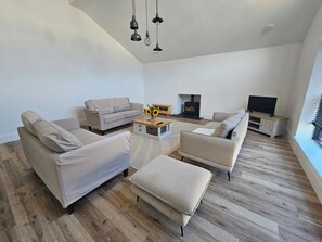 A modern living room with a sofa set, a coffee table with a vase of sunflowers, a fireplace, and a television on a stand. - Luxury Kent Bungalow Retreat Sleeps 12 (Tonbridge)