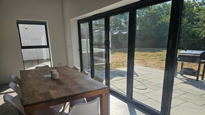 A modern dining area with a wooden table and chairs, large sliding glass doors leading to an outdoor patio. - Luxury Kent Bungalow Retreat Sleeps 12 (Tonbridge)