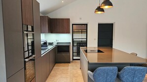A modern kitchen with dark wooden cabinets, a central island, and two bar stools. - Luxury Kent Bungalow Retreat Sleeps 12 (Tonbridge)