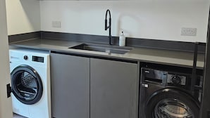 A compact kitchen with wooden cabinets, a built-in washing machine, and a dishwasher. - Luxury Kent Bungalow Retreat Sleeps 12 (Tonbridge)
