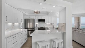 A modern kitchen with white cabinetry, a large island, stainless steel appliances, and a view of the ocean. - Luxury 3BR Beachfront Condo - Wrap Balcony, Endless Gulf Views! Pool & Beach! (Miramar Beach)