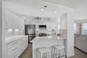 A modern kitchen with white cabinetry, a large island, stainless steel appliances, and a view of the ocean. - Luxury 3BR Beachfront Condo - Wrap Balcony, Endless Gulf Views! Pool & Beach! (Miramar Beach)