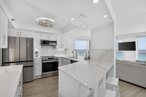A modern kitchen with stainless steel appliances, a marble countertop, and a view of the sea. - Luxury 3BR Beachfront Condo - Wrap Balcony, Endless Gulf Views! Pool & Beach! (Miramar Beach)