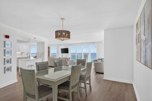 A modern interior with a dining area, kitchen, and living space with large windows overlooking the ocean. - Luxury 3BR Beachfront Condo - Wrap Balcony, Endless Gulf Views! Pool & Beach! (Miramar Beach)