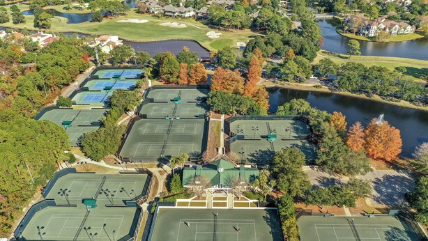 An aerial view of a tennis facility with multiple courts, surrounded by trees and a body of water. - Luxury 3BR Beachfront Condo - Wrap Balcony, Endless Gulf Views! Pool & Beach! (Miramar Beach)