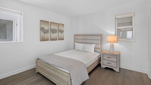 A bedroom with a bed, bedside table, lamp, and wall art. - Luxury 3BR Beachfront Condo - Wrap Balcony, Endless Gulf Views! Pool & Beach! (Miramar Beach)