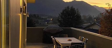 A balcony with a table and chairs, a barbecue grill, and a view of mountains.