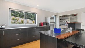A modern kitchen with dark cabinetry, a granite countertop, a built-in island with a sink, a refrigerator, and a microwave. - Wanaka 'Mount Iron Edge' with Mountain Views (Wanaka)