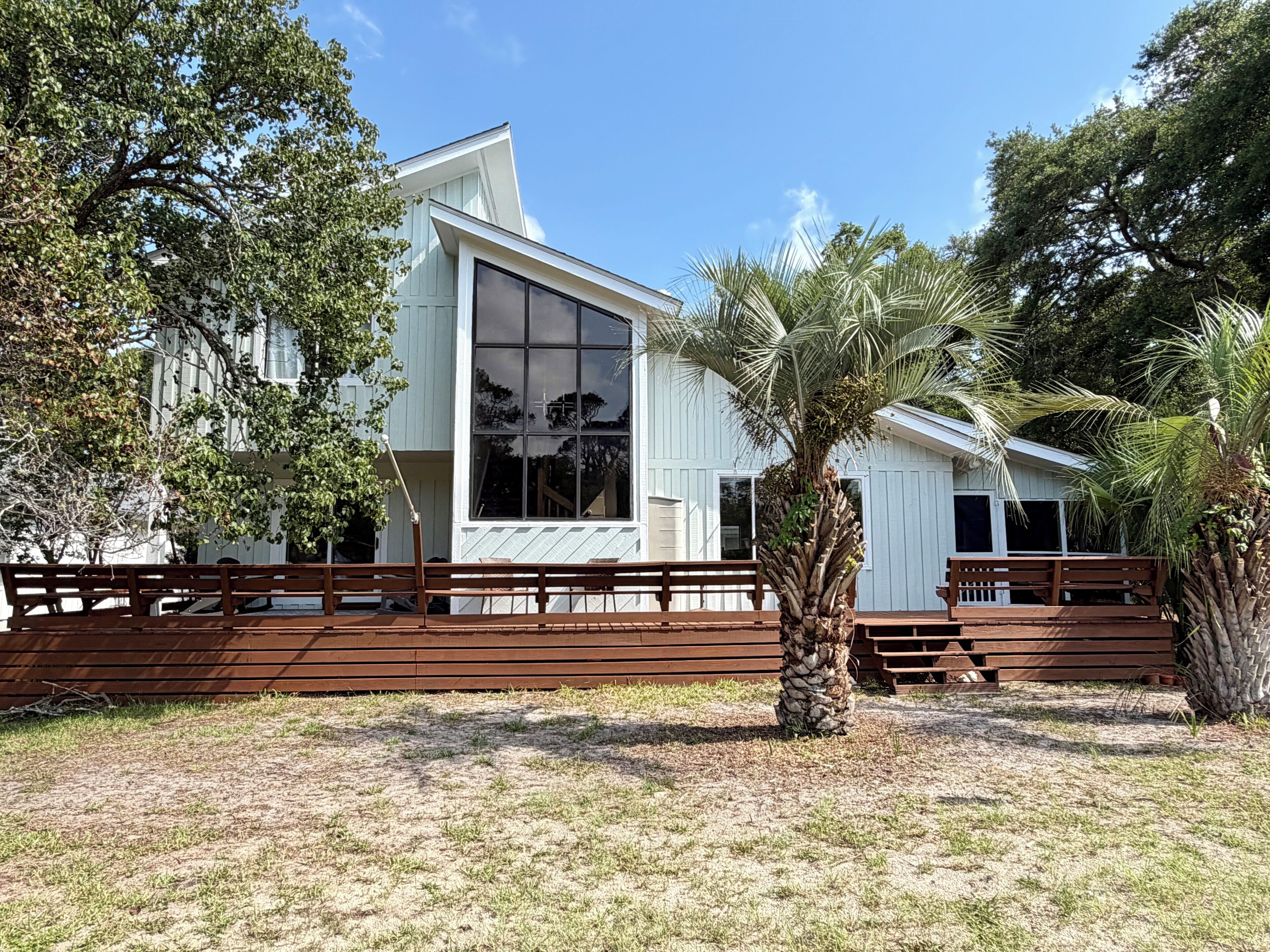 A modern white building with large windows, a wooden deck, and a palm tree.