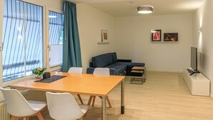 Uma sala de estar moderna com sofá, mesa de jantar com cadeiras, televisão e obras de arte nas paredes.