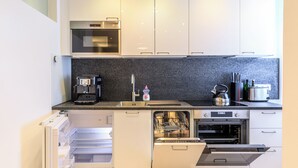 Cozinha moderna com armários brancos, forno embutido, máquina de lavar louça e cafeteira.