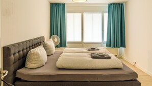 Quarto com cama, ventoinha e janela com cortinas.