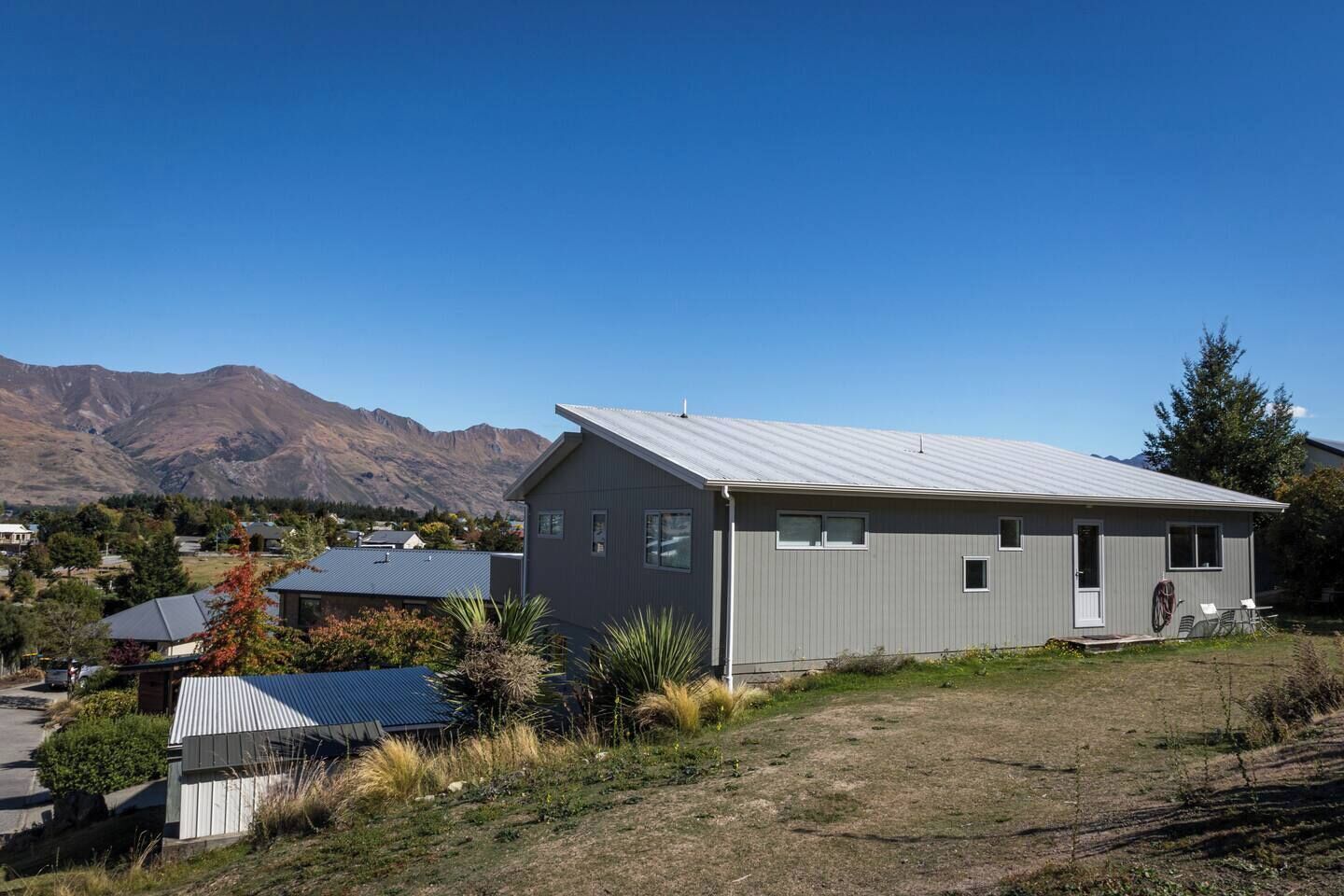A single-story building with a metal roof, surrounded by a grassy area and mountains in the background.