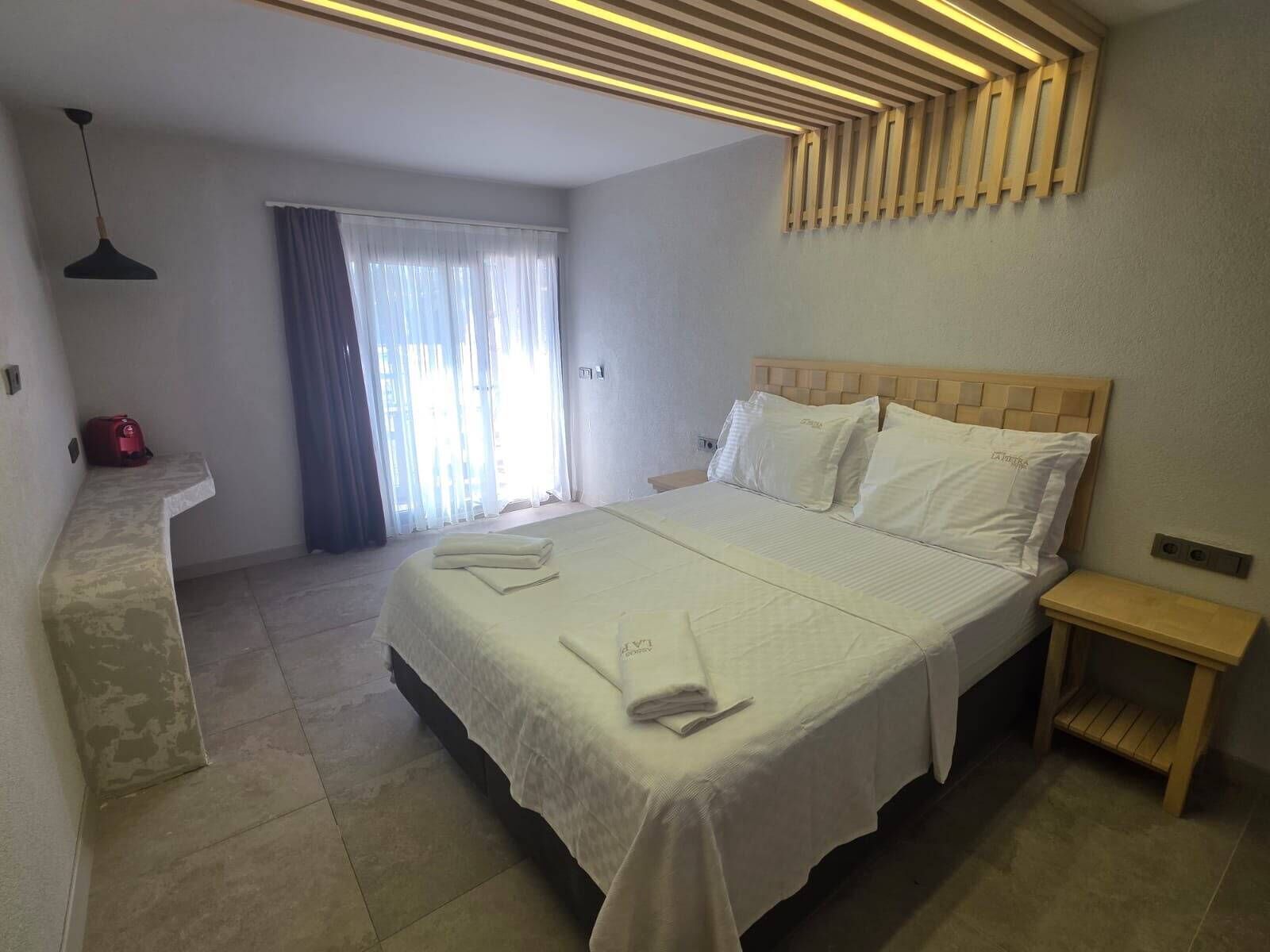 Habitació d'hotel amb llit, taules de nit, escriptori i finestra amb cortines.