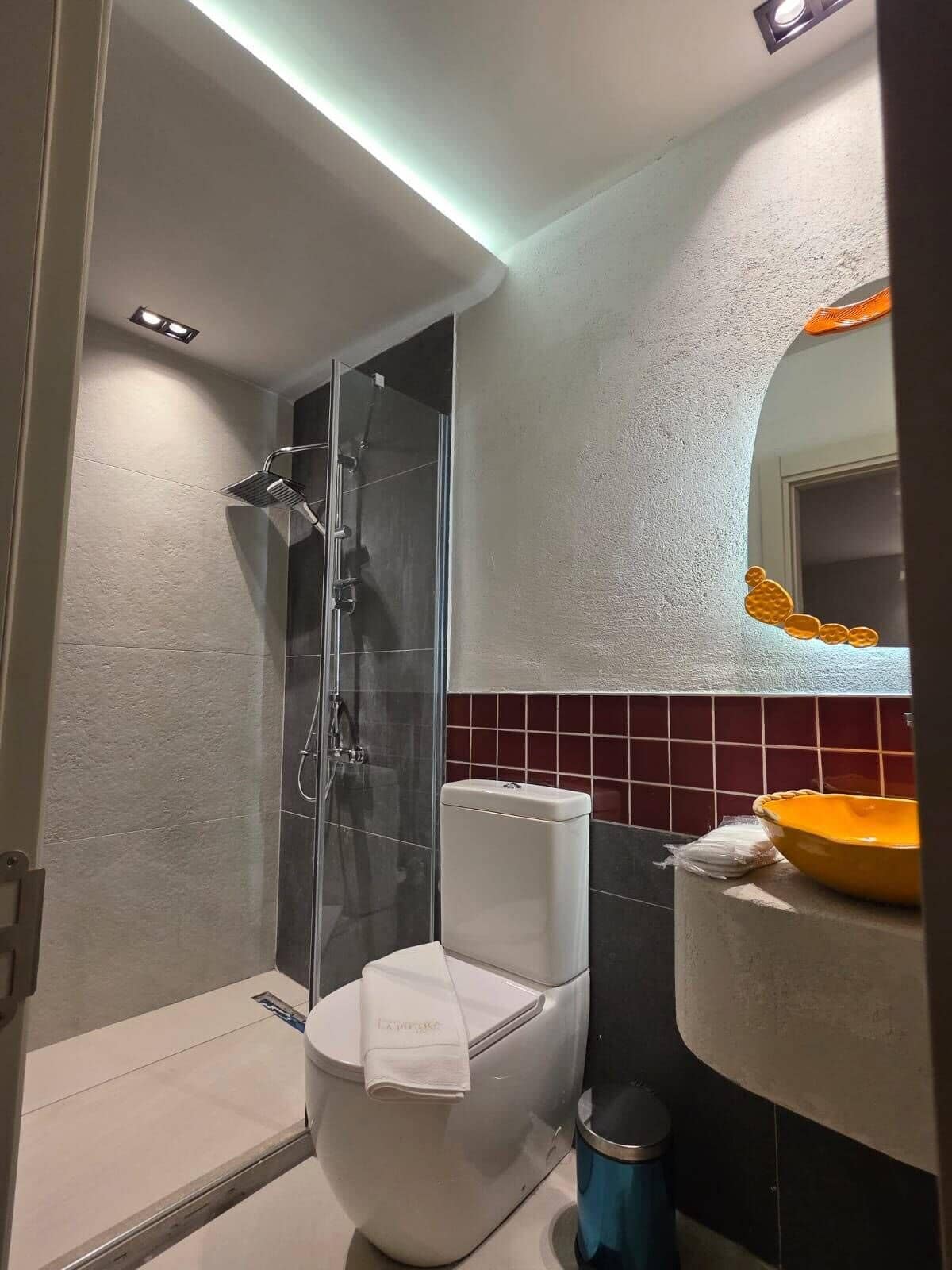 Une salle de bain moderne avec une douche à parois de verre, des toilettes blanches et un lavabo avec un receveur jaune.