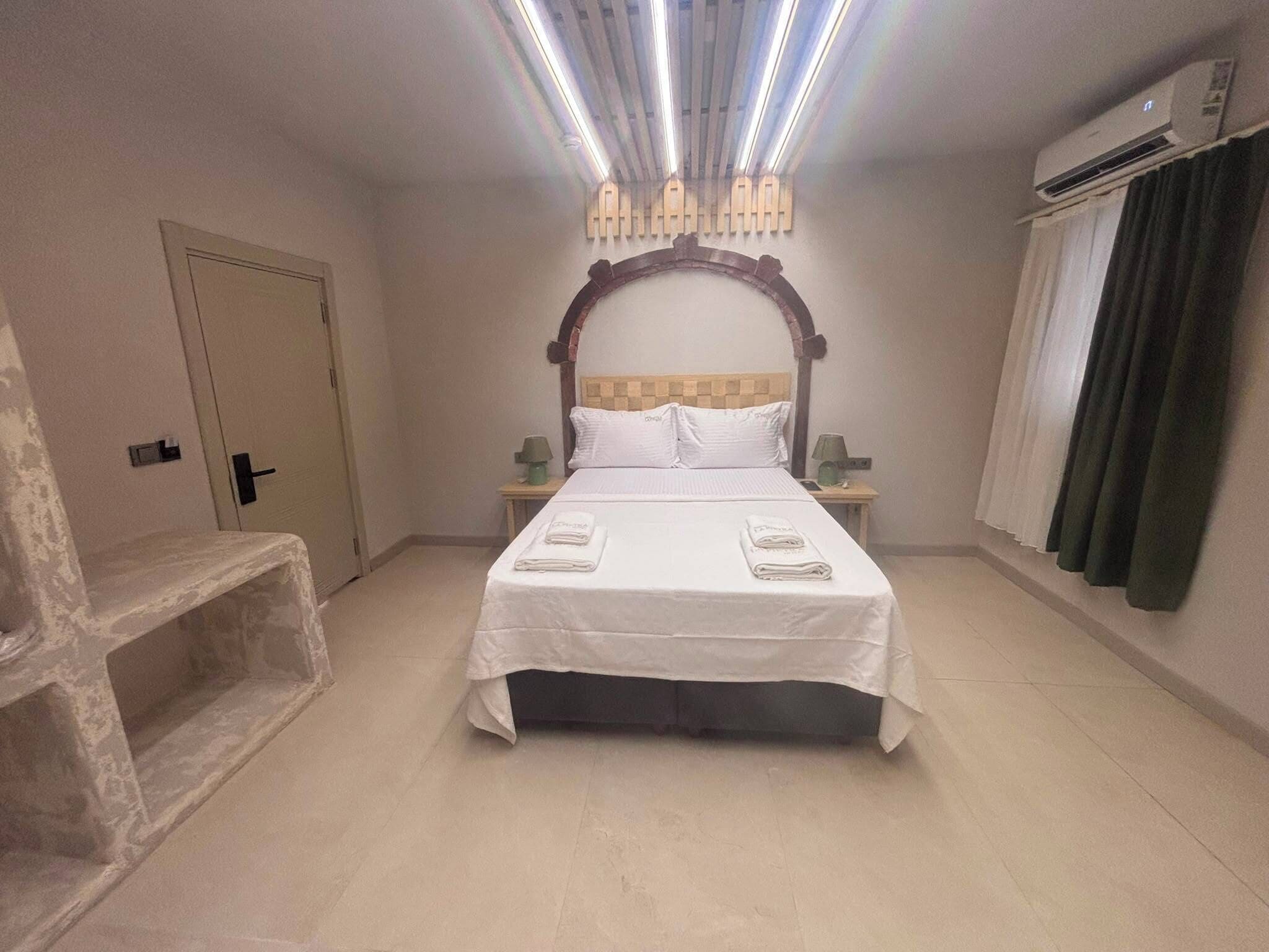 Habitación de hotel con cama, mesitas de noche, una puerta, equipo de aire acondicionado y una ventana con cortinas.