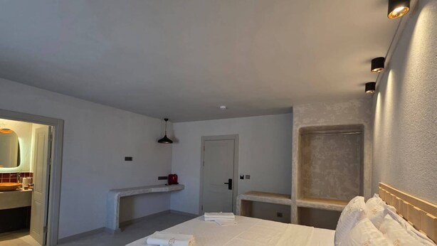 Una habitación de hotel con cama, mesita de noche, espejo y baño visible a través de una puerta abierta.
