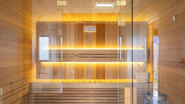 Une salle de bain moderne avec un lambris en bois, une cloison en verre, une colonne en marbre et un banc intégré.
