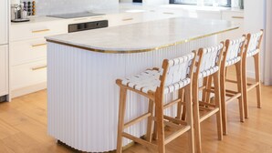 Une cuisine moderne dotée d’un îlot central, de luminaires suspendus et de chaises en bois.