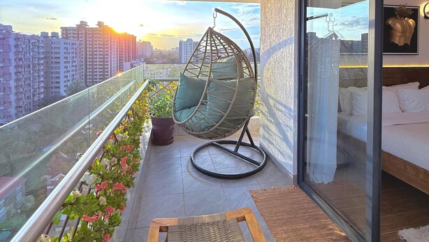 A balcony with a hanging chair, a small table, and a bed with a glass door. - Capital Rise View Palace Apartment (Nairobi)