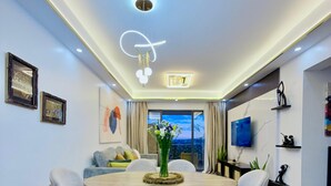 A modern dining area with a round table, six chairs, a vase of flowers, and a television on the wall. - Capital Rise View Palace Apartment (Nairobi)