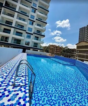 A swimming pool with blue mosaic tiles, surrounded by high-rise buildings. - Capital Rise View Palace Apartment (Nairobi)