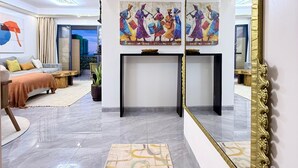 A modern hotel room with a large mirror, a sofa, a coffee table, a rug, and a painting on the wall. - Capital Rise View Palace Apartment (Nairobi)