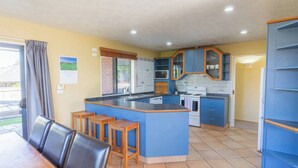 Een keuken met blauwe kastjes, een centraal eiland en een eethoek met een tafel en stoelen.