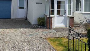 A residential property with a gravel driveway, a small front porch, a blue garage door, and a sign reading 'Westbury.' - PANORAMIC views in the heart of the Lakes, Keswick (Portinscale)