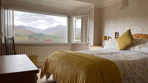 A bedroom with a large window, a bed with floral bedding, and a view of mountains. - PANORAMIC views in the heart of the Lakes, Keswick (Portinscale)