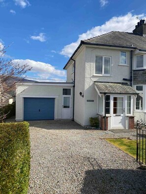 A two-story house with a blue garage door, a small front porch, and a gravel driveway. - PANORAMIC views in the heart of the Lakes, Keswick (Portinscale)
