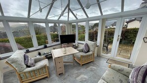 A conservatory with a glass ceiling, a wooden table, two chairs, and a sofa. - PANORAMIC views in the heart of the Lakes, Keswick (Portinscale)