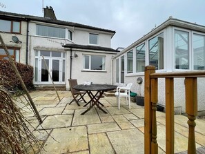 A patio with a round table and chairs, a wooden fence, and a house with large windows and a conservatory. - PANORAMIC views in the heart of the Lakes, Keswick (Portinscale)