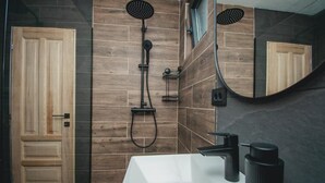 Un baño moderno con un espejo grande, una ducha con cabezal de mano y un lavabo blanco.