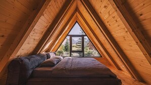 Un dormitorio acogedor en el ático con techo inclinado de madera, un ventanal grande y una cama con almohadas.