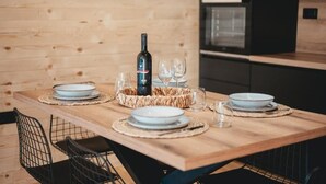 Una mesa de madera para comer con platos, vasos y una botella de vino, rodeada de cestas tejidas y sillas de alambre.