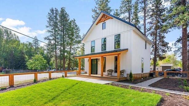 Een huis met twee verdiepingen, een overdekte veranda, een verzorgd gazon en een bebost achtergrond.