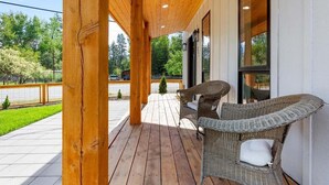 Een houten terras met rieten meubels, een kleine kerstboom en uitzicht op een groen landschap.
